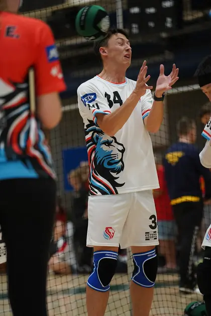 Dodgeball player in a gym, arms up, reacting as a green ball flies overhead.